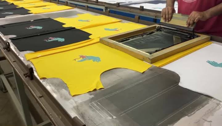 Screen printing station applying graphics to cut garment panels